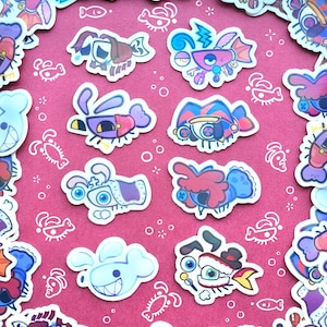 Può includere: Una collezione di adesivi in stile cartone animato raffiguranti vari pesci e creature marine stravaganti con occhi grandi, motivi vivaci e volti espressivi, disposti in un motivo circolare su uno sfondo magenta a tinta unita.