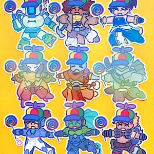 May include: A collection of nine die-cut stickers arranged in a grid, each featuring a different character wearing a colourful propeller hat and holding a vibrant rainbow-coloured lollipop. The characters display various outfits and armour designs.