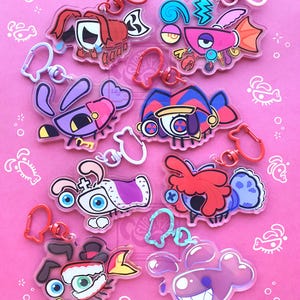 Pode incluir: Uma coleção de oito porta-chaves de acrílico com personagens de peixes de desenho animado coloridos e estilizados com expressões e acessórios únicos. Cada porta-chaves inclui um fecho em forma de peixe em várias cores, incluindo vermelho, rosa e azul-claro.