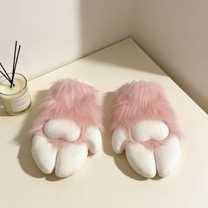 May include: A pair of plush pink and white paw-shaped mittens. The mittens have a fluffy pink fur exterior and white paw pads. The mittens are designed to resemble animal paws, with a soft, cuddly appearance.