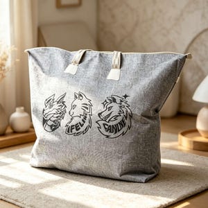 May include: A grey tote bag with a textured fabric finish featuring three black graphic illustrations of animal heads. The designs include a dragon, a cat with the text FELINE, and a wolf with the text CANINE. The bag has two light-colored handles.