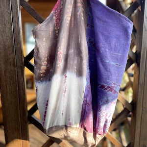 Könnte beinhalten: Eine große, handgefärbte Tragetasche mit Patchwork-Design. Die Tasche ist aus einem weichen, natürlichen Stoff gefertigt und hat eine Kombination aus lila, braunen und weißen Farben.