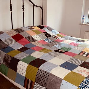 Könnte beinhalten: Eine Patchwork-Decke bestehend aus einem Raster aus quadratischen Stoffstücken in verschiedenen Farben, darunter Blau-, Rosa-, Grün-, Braun- und Weißtöne. Die Decke zeigt eine Mischung aus einfarbigen Stoffen, Blumenmustern, Streifen und geometrischen Designs.
