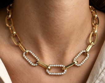 May include: A gold chain necklace featuring large oval links. Three of the central links are embellished with small, clear, sparkling stones set along the entire perimeter of each link, creating a contrast with the plain gold links.