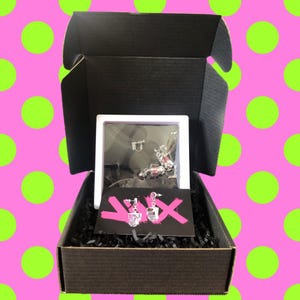 May include: A black box with a white box inside. The white box contains a pair of silver earrings with pink and clear stones. The earrings are on a black and pink card with the text "YIX" on it.