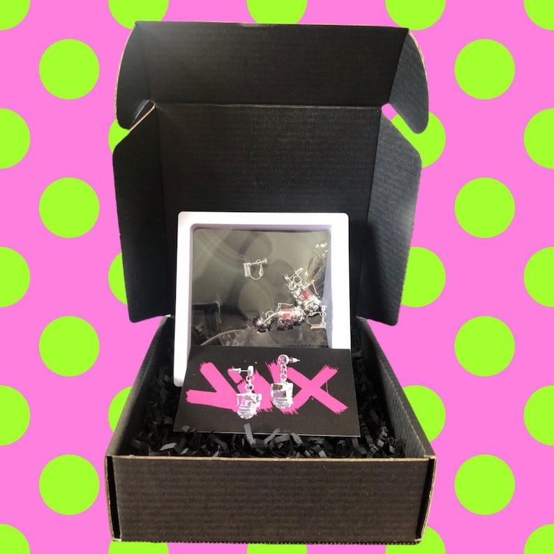 May include: A black box with a white box inside. The white box contains a pair of silver earrings with pink and clear stones. The earrings are on a black and pink card with the text "YIX" on it.