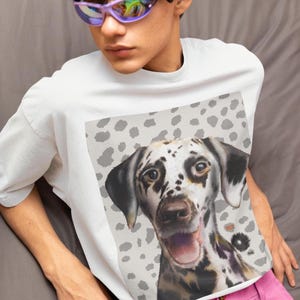 Könnte beinhalten: Weißes T-Shirt mit einem Dalmatiner-Hund, der fröhlich lächelt. Der Hund hat schwarze Flecken auf weißem Fell. Der Hintergrund ist hellgrau mit dunkleren grauen Flecken. Das T-Shirt hat eine lockere Passform.