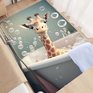 May include: A light blue bath mat featuring a cartoon giraffe in a bathtub surrounded by bubbles. The giraffe is brown and white against a light blue background.