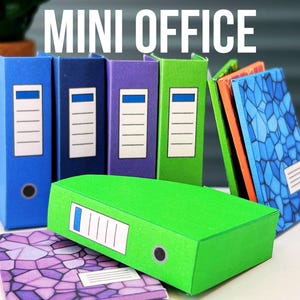 Op de afbeelding: Een set miniatuurkantoorartikelen, waaronder blauwe, groene, paarse en oranje mappen met een patroon. De mappen zijn in een rij op een tafel gerangschikt. De tekst "MINI OFFICE" is in witte letters op een zwarte achtergrond boven de mappen geschreven.
