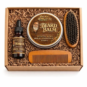 May include: A grooming gift set in a cardboard box containing a 1 fl oz bottle of Village Homestead beard oil, a round tin of beard balm with shea butter, beeswax, jojoba oil, meadowfoam oil, and vitamin E, a wooden beard comb, and a brush.