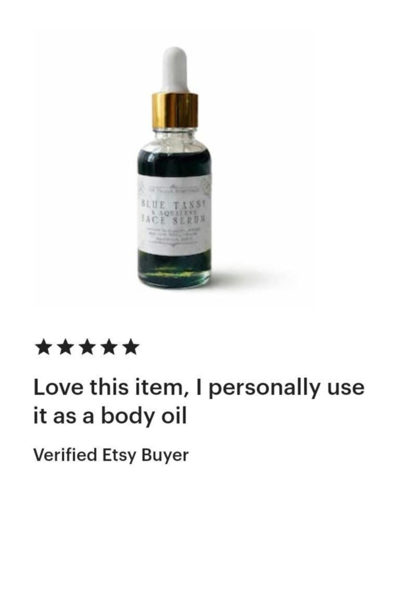 Pu&ograve; includere: Un flacone contagocce in vetro trasparente riempito con un liquido blu scuro. Il flacone presenta un colletto dorato, un tappo contagocce bianco e un'etichetta bianca con testo nero che recita Blue Tansy & Squalane Face Serum in carattere serif.