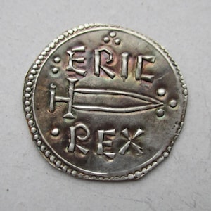 May include: A silver coin with a raised design of a sword and the inscription "ERIC REX".
