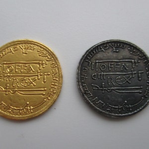 May include: Two coins, one gold and one silver, both inscribed with "OFFA REX". These coins date back to the reign of Offa of Mercia, an Anglo-Saxon king who ruled from 757 to 796.