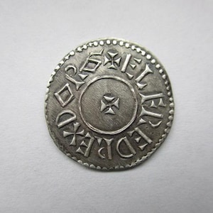 May include: A silver coin with embossed text and cross symbols. The coin has a circular design with a beaded border. The text appears to be in an older script, and the coin has a worn appearance.
