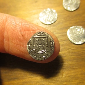 May include: A silver coin with a portrait of a person wearing a crown and a necklace. The coin has a raised rim and is slightly worn.