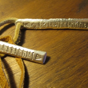 May include: Two silver pendants with leather cord, each with a different inscription in runes. The top pendant has the inscription "Fylgja" and the bottom pendant has the inscription "Mimir".