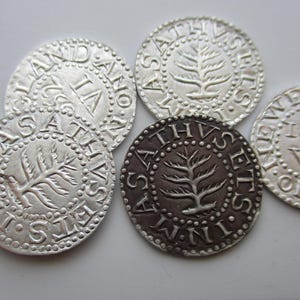 May include: A collection of antique silver coins, some with a dark patina. Each coin features embossed text and a central tree design. The coins are arranged on a light surface, showcasing their intricate details and historical significance.