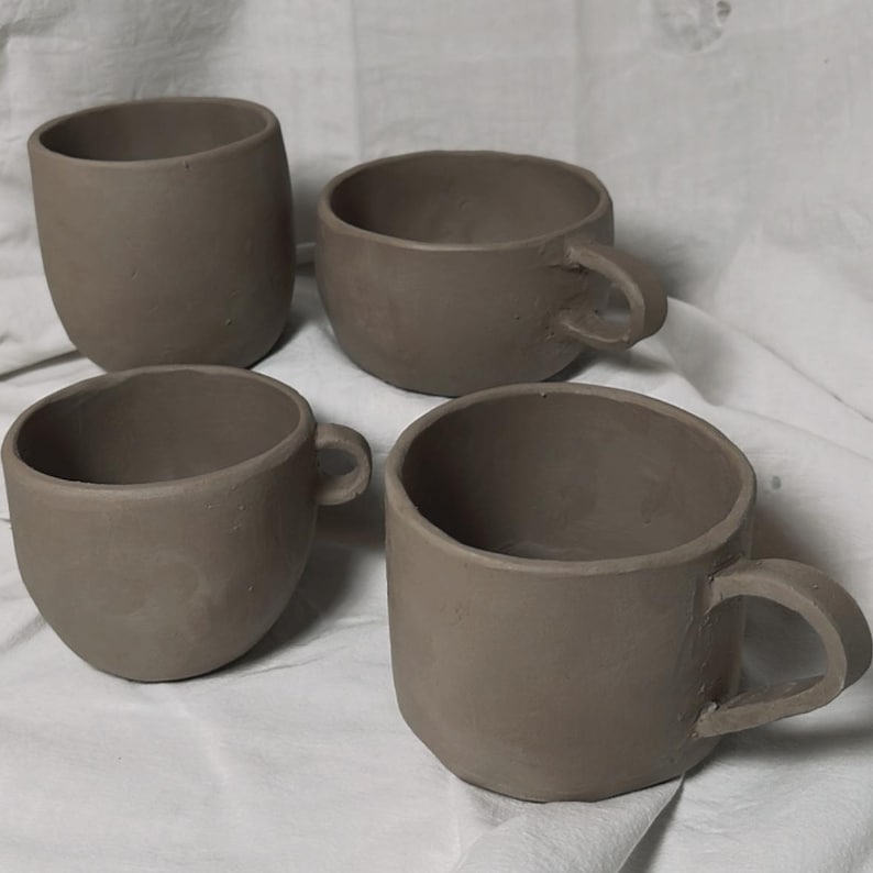 May include: Four brown ceramic mugs with handles. The mugs are unglazed and have a rustic appearance.