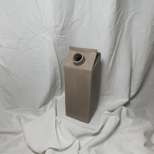 May include: A light brown ceramic vase shaped like a milk carton.