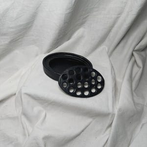 Op de afbeelding: Zwarte keramische schaal met een cirkelvormig uitsparingenpatroon. De schaal is gemaakt van glad, matzwart keramiek en heeft een eenvoudig, modern ontwerp.