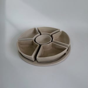 May include: A circular beige ceramic serving tray featuring five removable wedge-shaped compartments arranged around a single central circular bowl. The entire set is finished in a smooth, matte, light tan glaze with clean, defined edges.