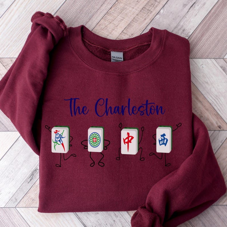 May include: Burgundy sweatshirt with the text "The Charleston" in blue lettering and a graphic of four cartoon figures holding mahjong tiles.