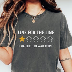 May include: Dark gray t-shirt with the text "LINE FOR THE LINE" and a rating of one gold star out of five. The shirt also says "I WAITED... TO WAIT MORE."
