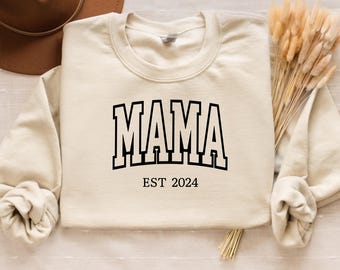 May include: A cream-colored sweatshirt with the text "MAMA EST 2024" printed in black.