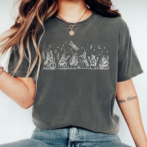 May include: Dark grey t-shirt with a white illustration of insects playing instruments. The design includes a dragonfly, musical notes, and stars. The shirt is made of a soft, comfortable material.