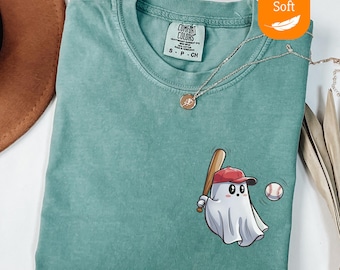 May include: Light green t-shirt with a baseball-themed ghost graphic. The ghost wears a red baseball cap and holds a bat, with a baseball nearby. The shirt has a crew neck and a small tag.