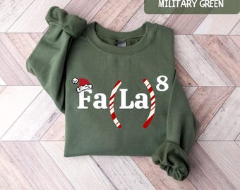May include: A green sweatshirt with the text "Fa La" and a candy cane design. The text is in white and the candy canes are red and white. The sweatshirt is a Christmas themed design.