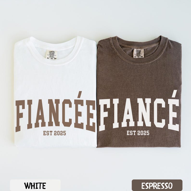 K&ouml;nnte beinhalten: Zwei gefaltete T-Shirts, eines wei&szlig; und eines espressofarben, mit den W&ouml;rtern "FIANC&Eacute;E" und "FIANC&Eacute;" in Braun bzw. Wei&szlig; bedruckt. Der Text "EST 2025" steht darunter. Das wei&szlig;e Shirt hat ein wei&szlig;es Etikett mit der Aufschrift "WHITE" und das Espresso-Shirt ein Etikett mit der Aufschrift "ESPRESSO".