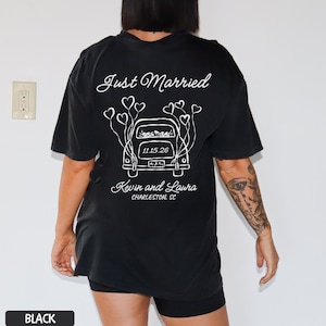 May include: Black t-shirt with a white graphic design on the back. The design features the words "Just Married" above a car illustration with heart-shaped balloons. Below the car are the names "Kevin and Laura" and the location "Charleston, SC".