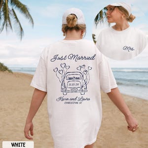 May include: White t-shirt with a navy blue graphic that says "Just Married" and features a car with heart-shaped balloons. The shirt also includes the names "Kevin and Laura" and the date "11.15.26" and the location "Charleston SC".
