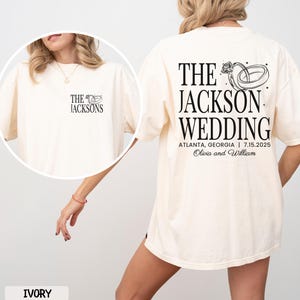 May include: Ivory t-shirt featuring black text and a wedding ring graphic. The front displays "THE JACKSONS" with a ring graphic. The back reads "THE JACKSON WEDDING" with the wedding date and location.