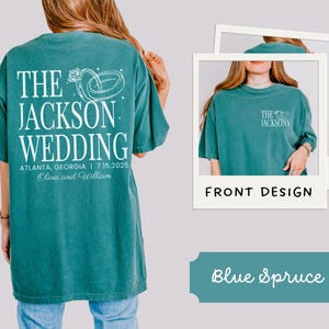 May include: Teal t-shirt with white text and graphic. The back of the shirt says "THE JACKSON WEDDING" with the date and location. A smaller design is on the front. The shirt is labelled "Blue Spruce".