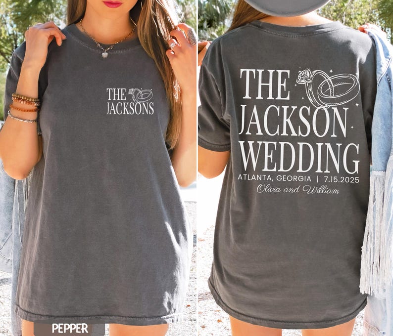 May include: Dark grey t-shirt featuring white text and a wedding ring design. The front displays "The Jacksons." The back reads "The Jackson Wedding" with the date, location, and couple's names.