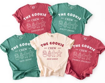 May include: Five t-shirts in various colors, including red, green, and cream. Each shirt features the text "THE COOKIE CREW" with different job titles like "Dough Roller" and "Sprinkle Specialist" and the year 2025.