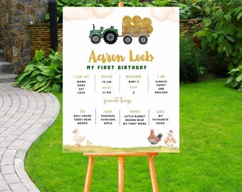 May include: A personalized birthday sign on an easel, featuring a green tractor pulling a hay wagon. The sign includes the name "Aaron Loeb" and details about the child's first birthday, with a green and gold color scheme.