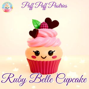 Puede incluir: Un cupcake rosa y rojo con una cara sonriente, decorado con una frambuesa, hojas verdes y corazones de chocolate. El cupcake está sobre un fondo blanco con estrellas blancas. El texto "Puff Puff Pastries" y "Ruby Belle Cupcake" es visible en la imagen.