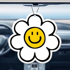 May include: A white flower-shaped car air freshener with a yellow smiley face in the center.