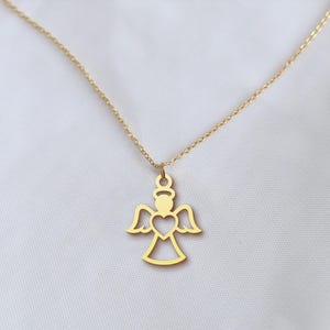 Op de afbeelding: Een goudkleurige ketting met een engel hanger. De hanger heeft een halo, vleugels en een hartvormige uitsparing. De delicate gouden ketting staat tegen een witte achtergrond. Het engelontwerp is een eenvoudig, elegant silhouet.