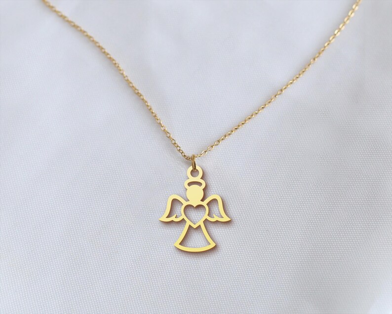 Op de afbeelding: Een goudkleurige ketting met een engel hanger. De hanger heeft een halo, vleugels en een hartvormige uitsparing. De delicate gouden ketting staat tegen een witte achtergrond. Het engelontwerp is een eenvoudig, elegant silhouet.