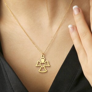 Op de afbeelding: Een gouden engel hanger ketting. De hanger heeft een engelen silhouet met een hart. De ketting wordt gedragen door een persoon die een zwart shirt draagt.