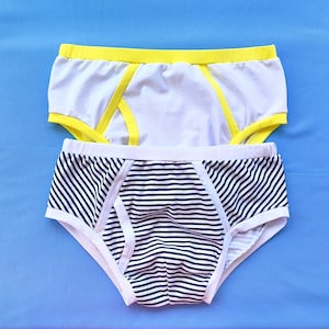 Può includere: Due paia di slip impilate verticalmente. Il paio superiore è bianco tinta unita con bordi e fascia in vita giallo brillante. Il paio inferiore presenta un motivo a righe orizzontali blu navy e bianco con bordi e fascia in vita bianchi.