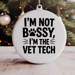 May include: White round Christmas ornament with the text "I'M NOT BOSS, I'M THE VET TECH" in black. The word "BOSS" is replaced with a paw print. A gold string is attached for hanging.