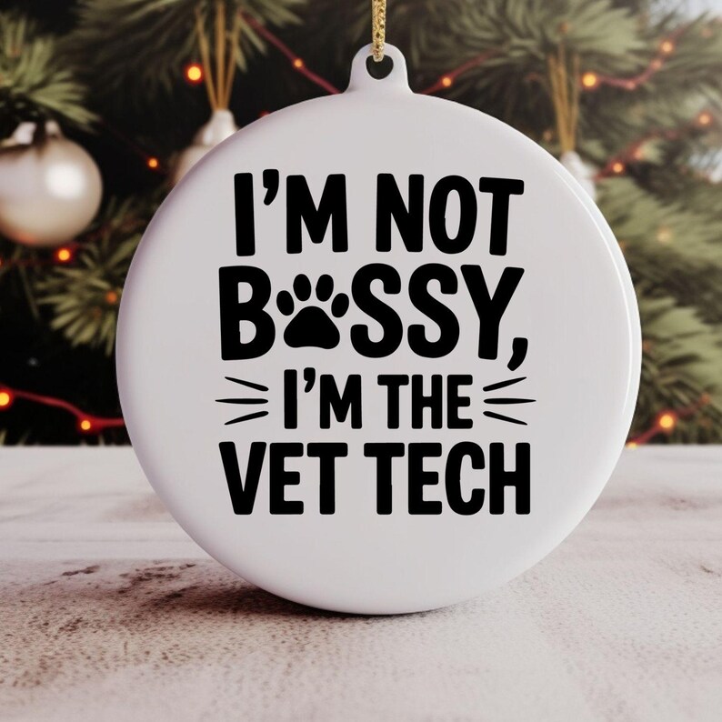 May include: White round Christmas ornament with the text "I'M NOT BOSS, I'M THE VET TECH" in black. The word "BOSS" is replaced with a paw print. A gold string is attached for hanging.