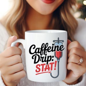 May include: White ceramic mug with the words "Caffeine Drip: STAT!" in black and red. The mug features a graphic of an IV drip bag with red liquid, blue liquid, and a black tube. The mug has a white handle.