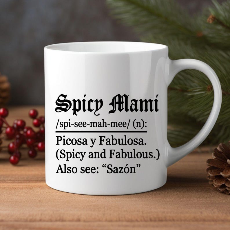 May include: White ceramic mug with the text "Spicy Mami" in a decorative font. Below the title is the phonetic pronunciation, followed by the Spanish translation "Picosa y Fabulosa" and the English translation "Spicy and Fabulous."