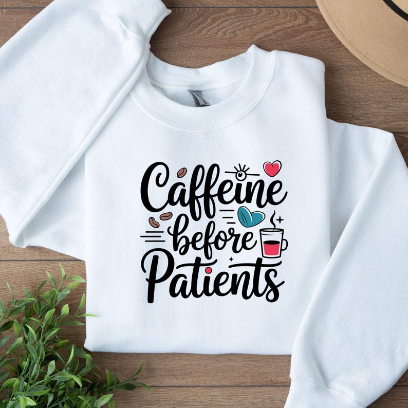 May include: White crewneck sweatshirt with the text "Caffeine before Patients" in black script. The design includes coffee beans, a heart, and a coffee cup. The sweatshirt is made of a soft material.
